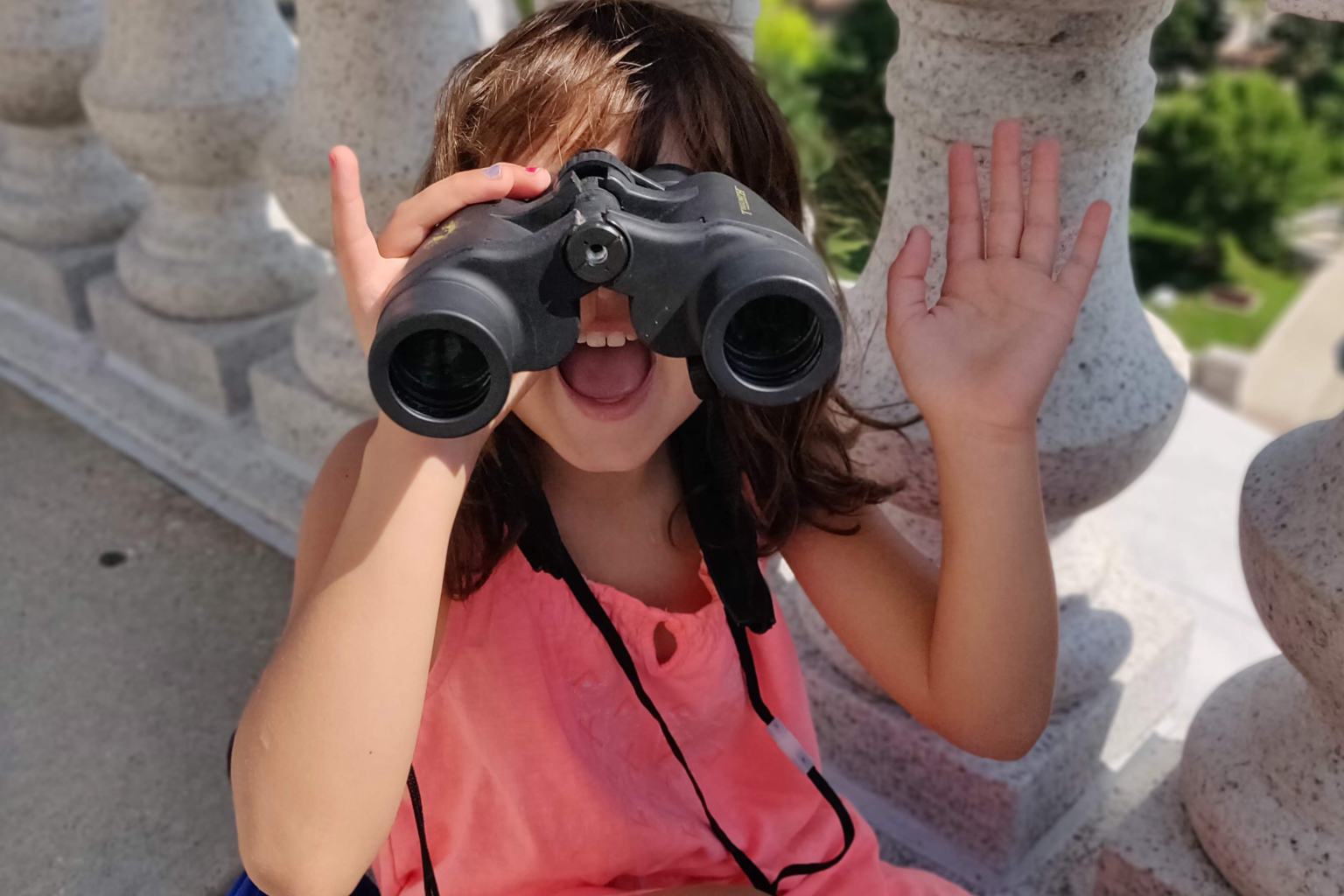 a small girl waves to the camera while looking through binoculars